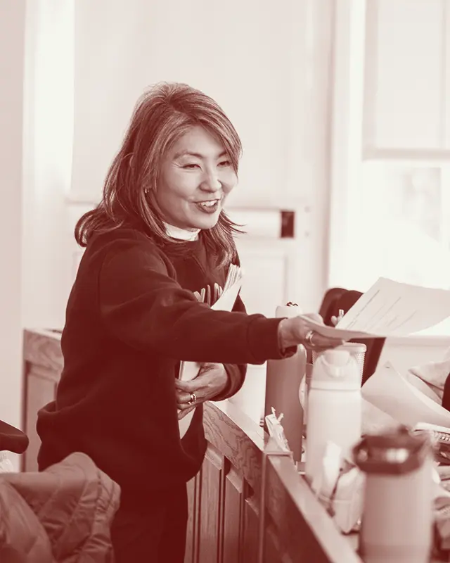 May Young in a classroom setting, smiling as she hands a paper to a student.